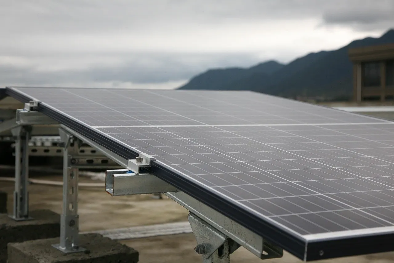 Ein schräg aufgeständertes Solarmodul mit Aluminiumrahmen auf einem Metallgestell, im Hintergrund bewölkter Himmel und Berge