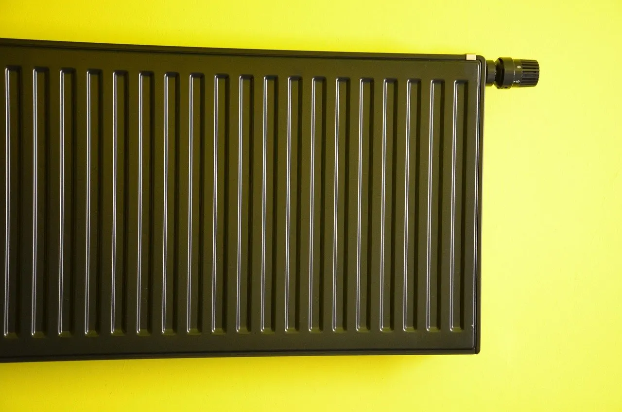 Dunkler Plattenheizkörper mit Thermostatkopf an der rechten oberen Ecke, montiert vor einer leuchtend gelben Wand