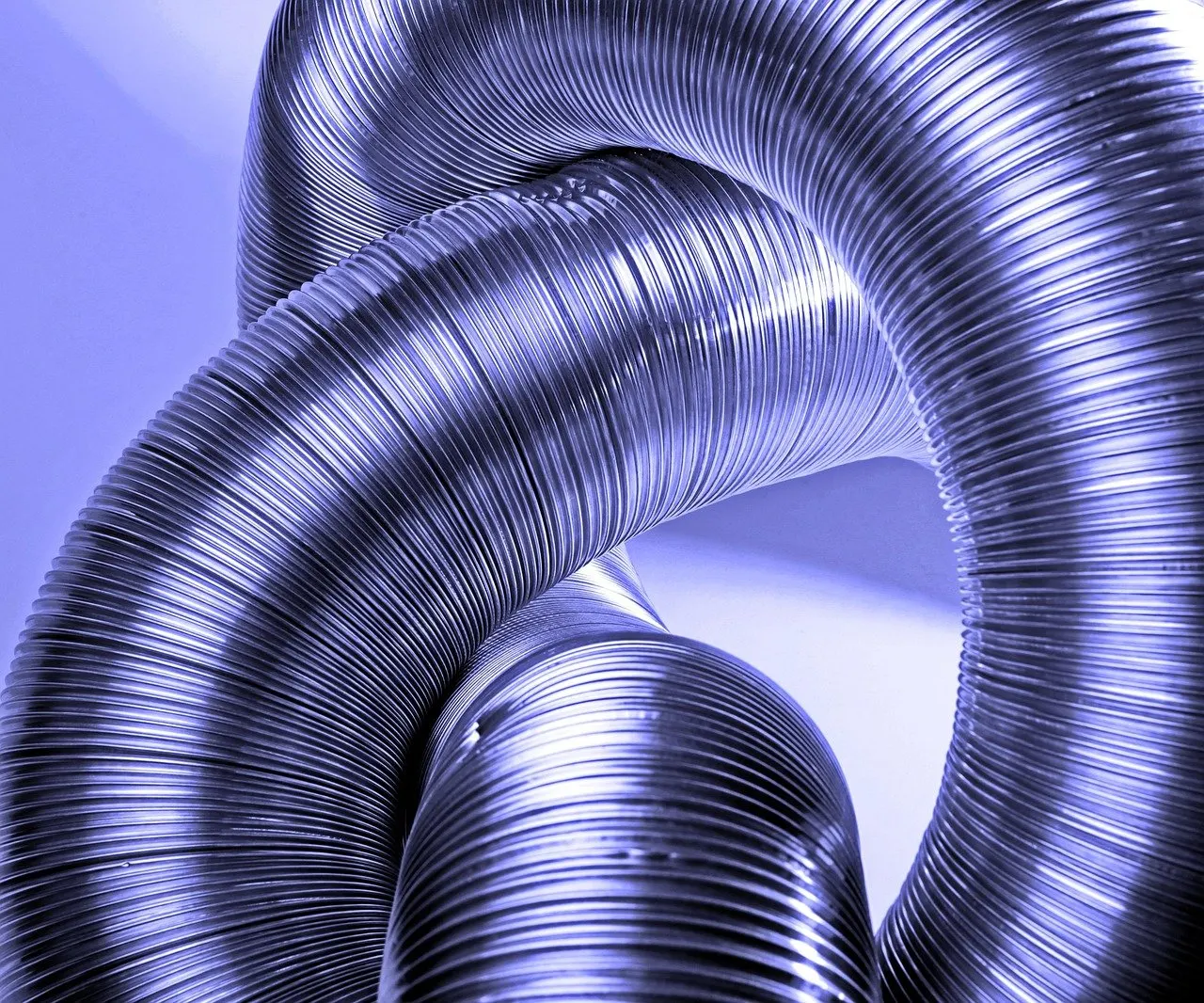 Mehrere flexible Lüftungsrohre aus gerilltem Aluminium, die sich ineinander verschlingen, in bläulichem Licht fotografiert