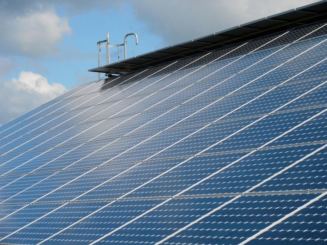 Schrägdach vollständig mit blauen Solarmodulen belegt, am First ein Dachausstieg mit Metallbügeln, darüber Wolken