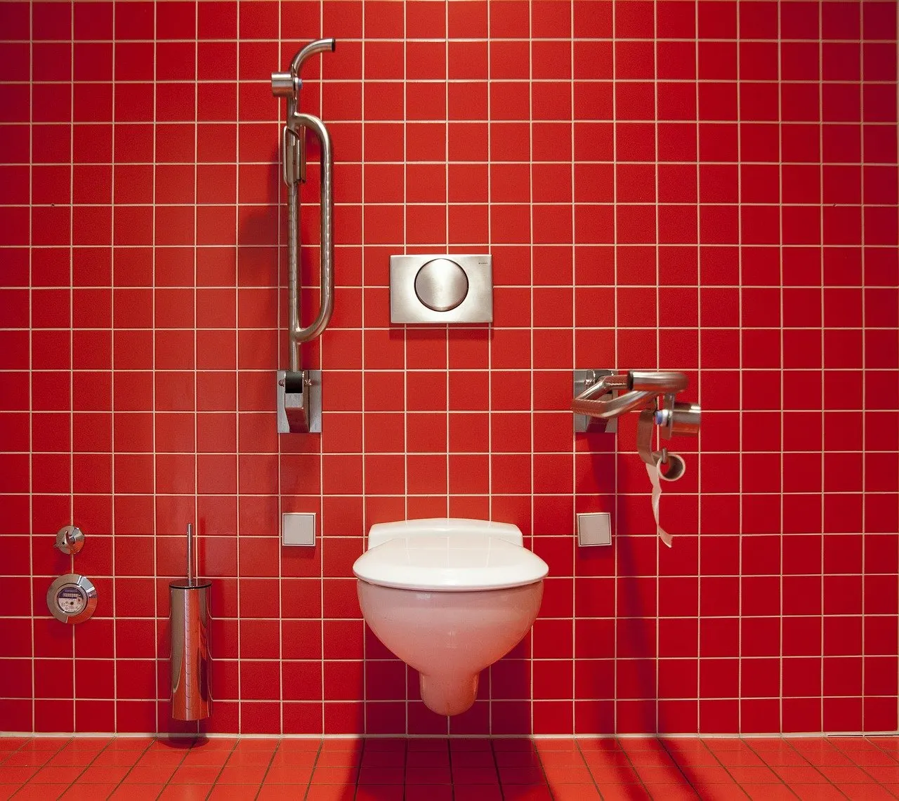 Wand-WC an rot gefliester Wand, darüber eine runde Betätigungsplatte des Unterputzspülkastens, links und rechts Haltegriffe