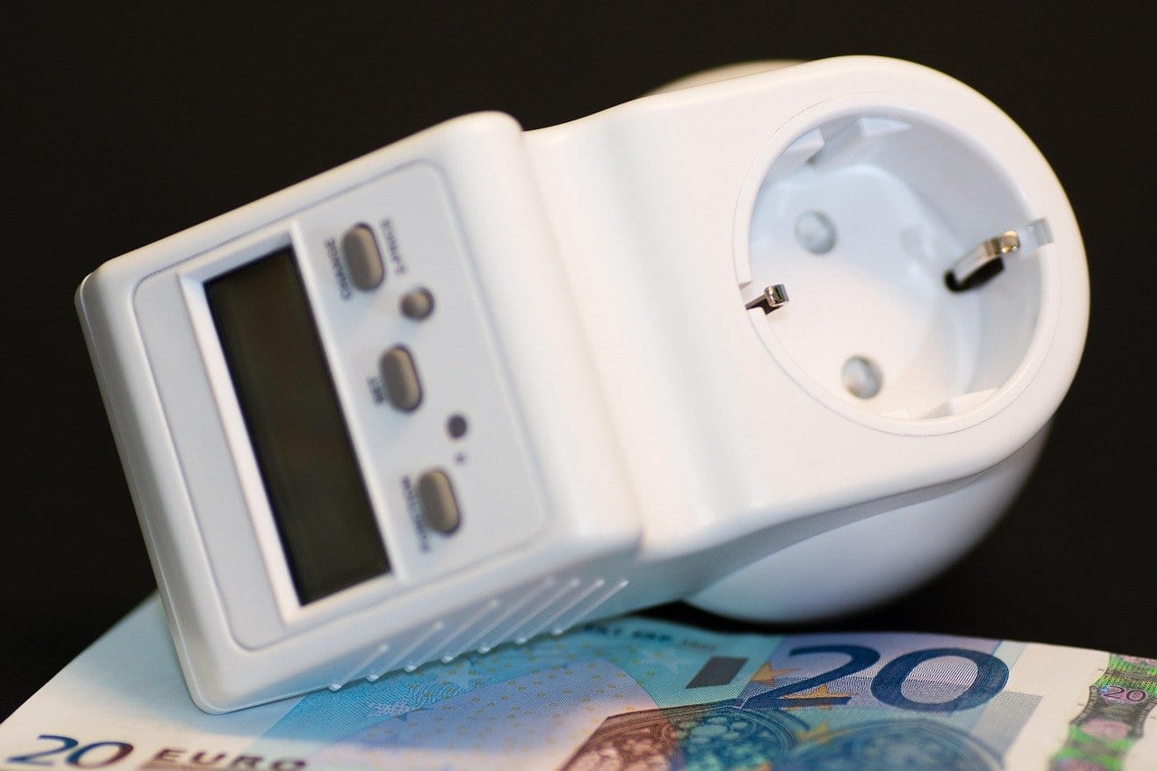 Weißes Strommessgerät für die Steckdose mit Display und drei Tasten, liegend auf einem 20-Euro-Schein